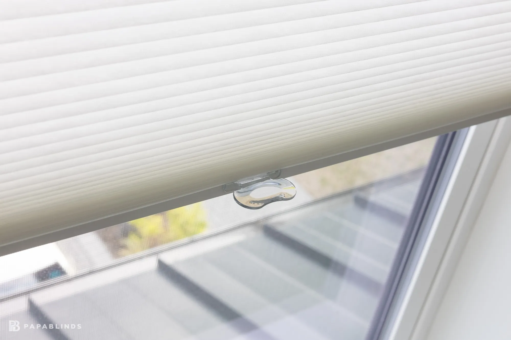 Close-up of the clear lift handle on the rail of a white cellular shade